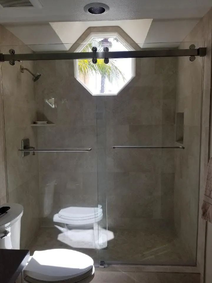Glass shower enclosure with stone tile walls, a skylight, and a toilet visible beyond the door.
