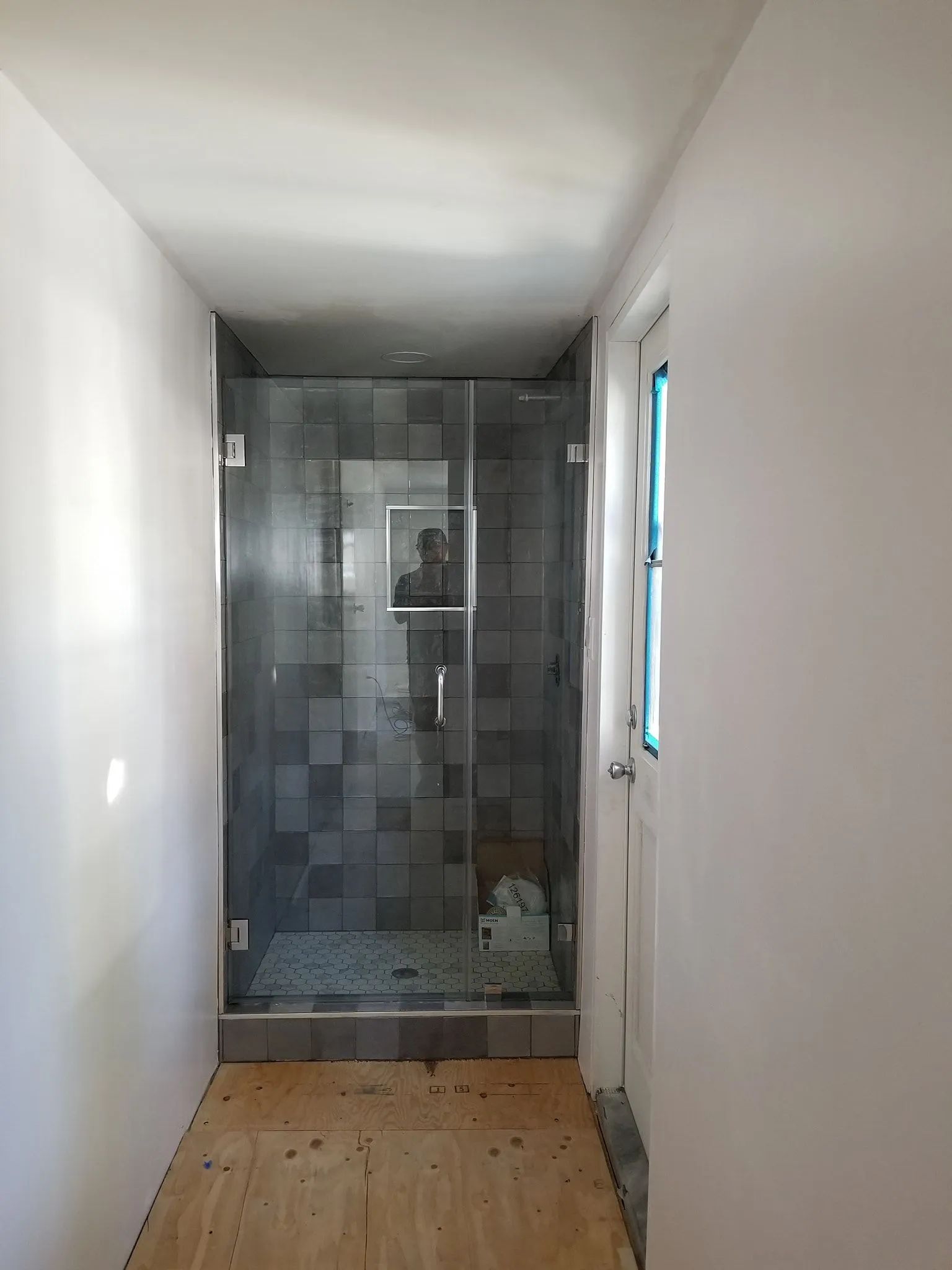 Narrow hallway with a wooden floor leading to a tiled shower or bathroom at the end