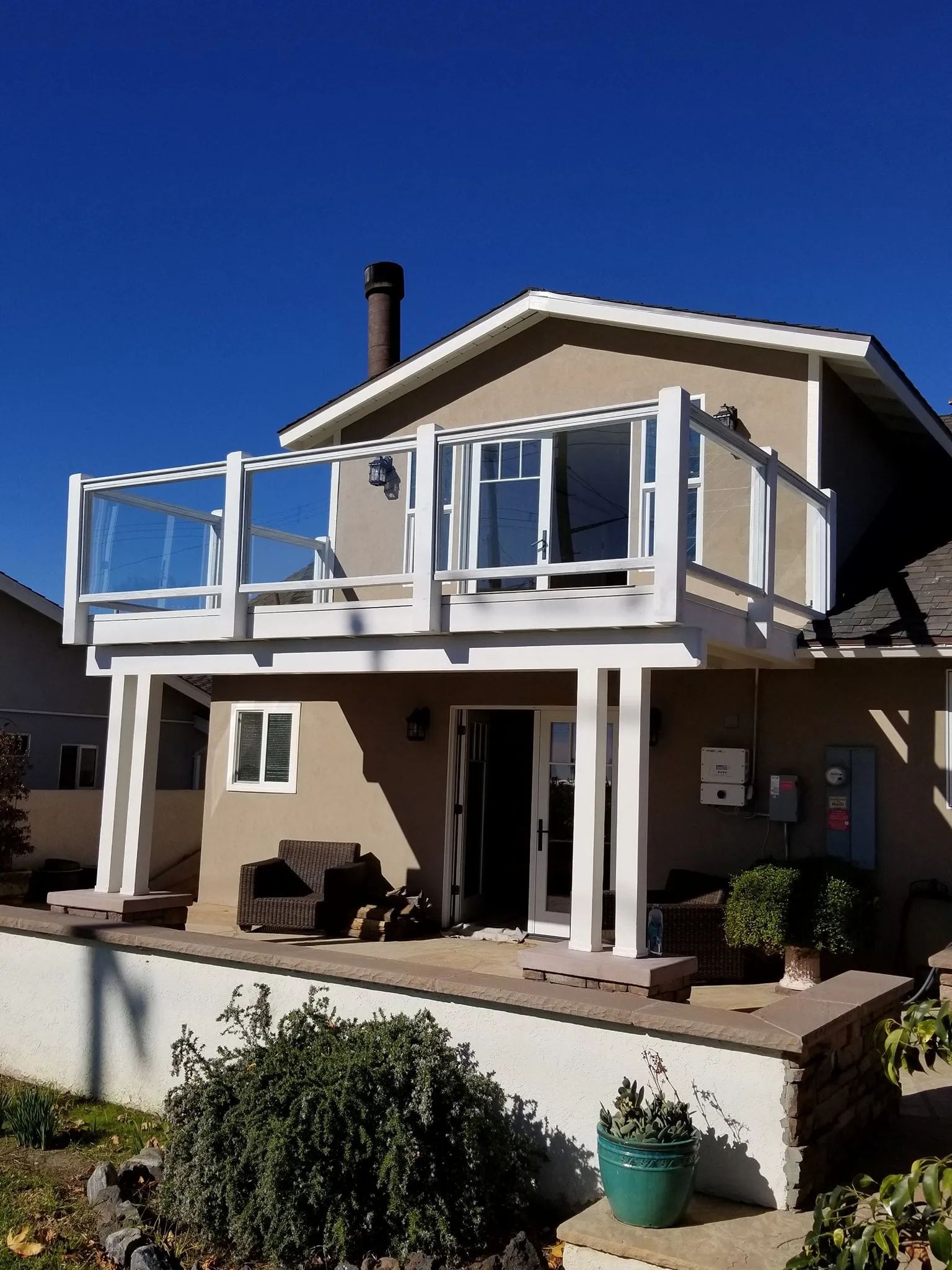 Two-story beige house with a balcony, white trim, and a front patio under a clear blue sky