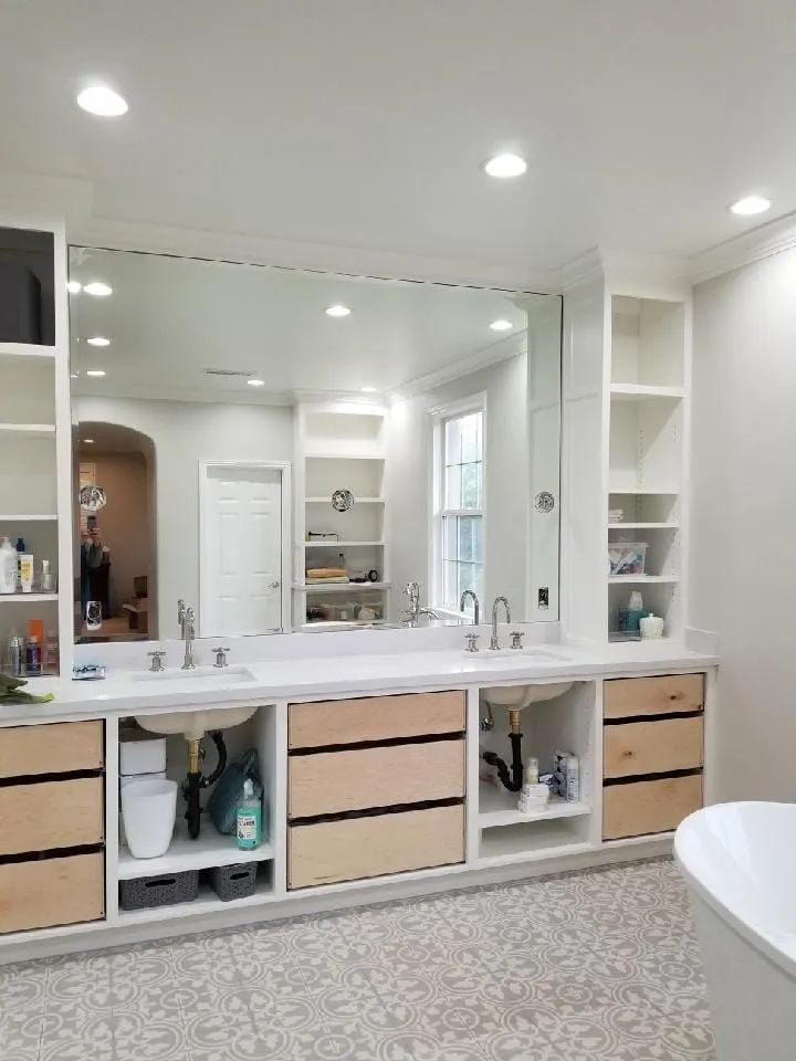 Bright bathroom with large mirror, double sink vanity, open storage cubbies, and white tiled floor