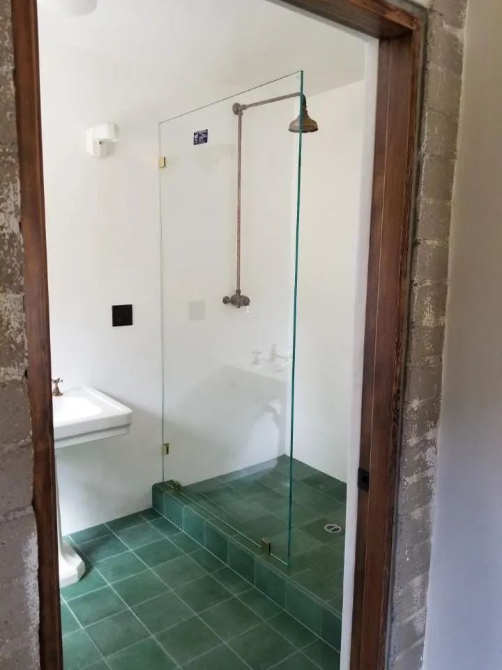 Small bathroom with a green-tiled walk-in shower and clear glass door beside a sink