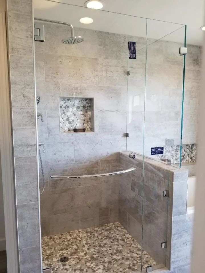 Glass walk-in shower with beige tile, pebble floor, built-in bench, and niche shelves