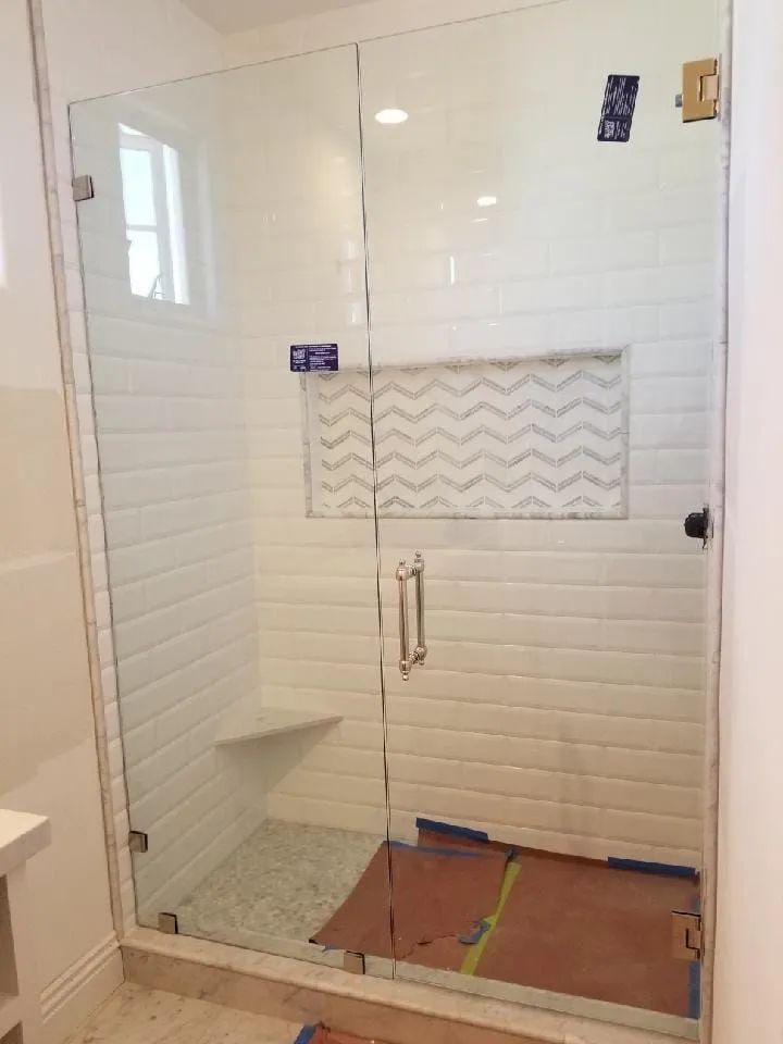 Glass shower enclosure with tiled walls and a built-in bench, seen in a bathroom under construction.