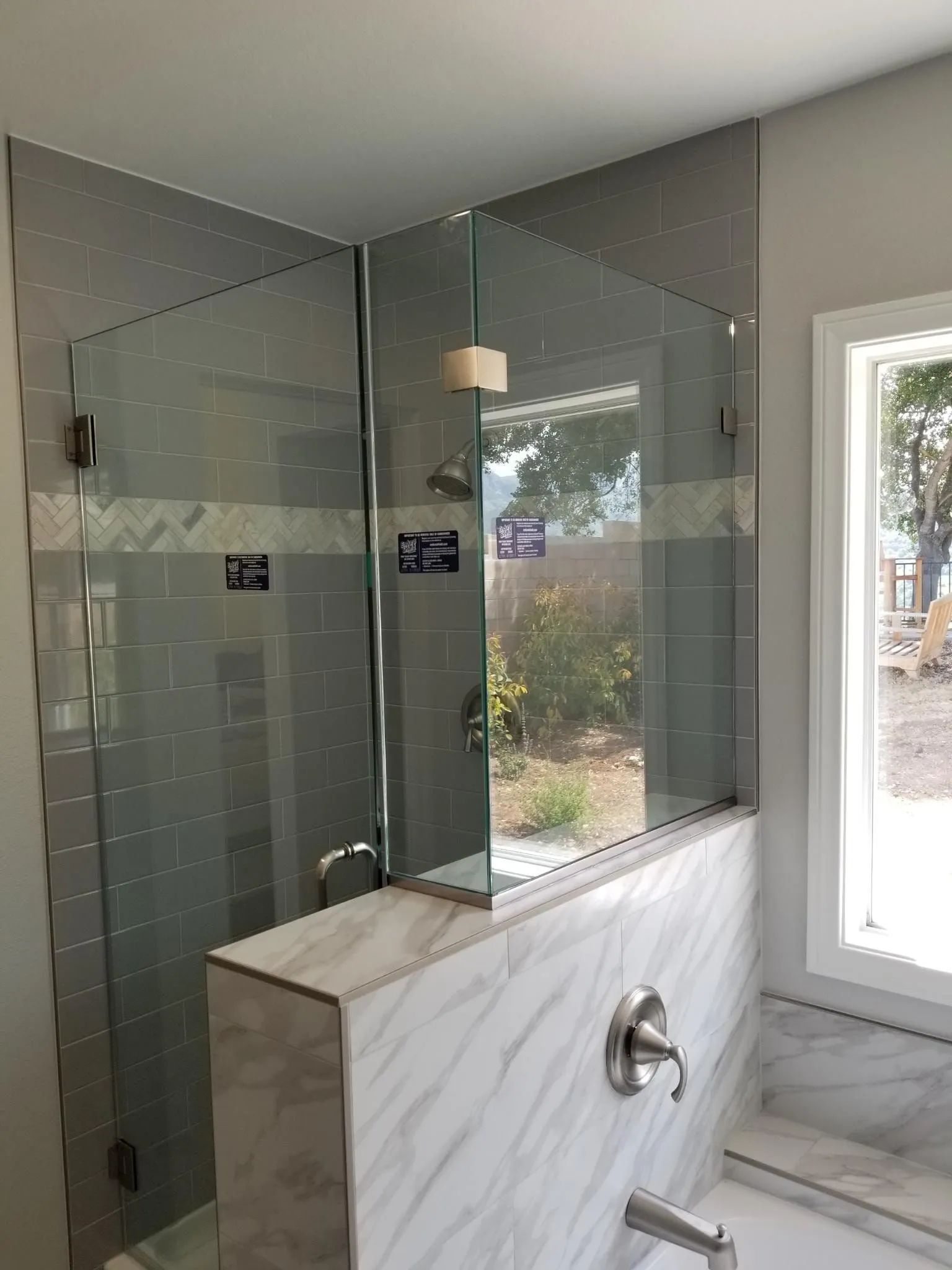 Modern bathroom with glass shower enclosure, marble vanity, and window light