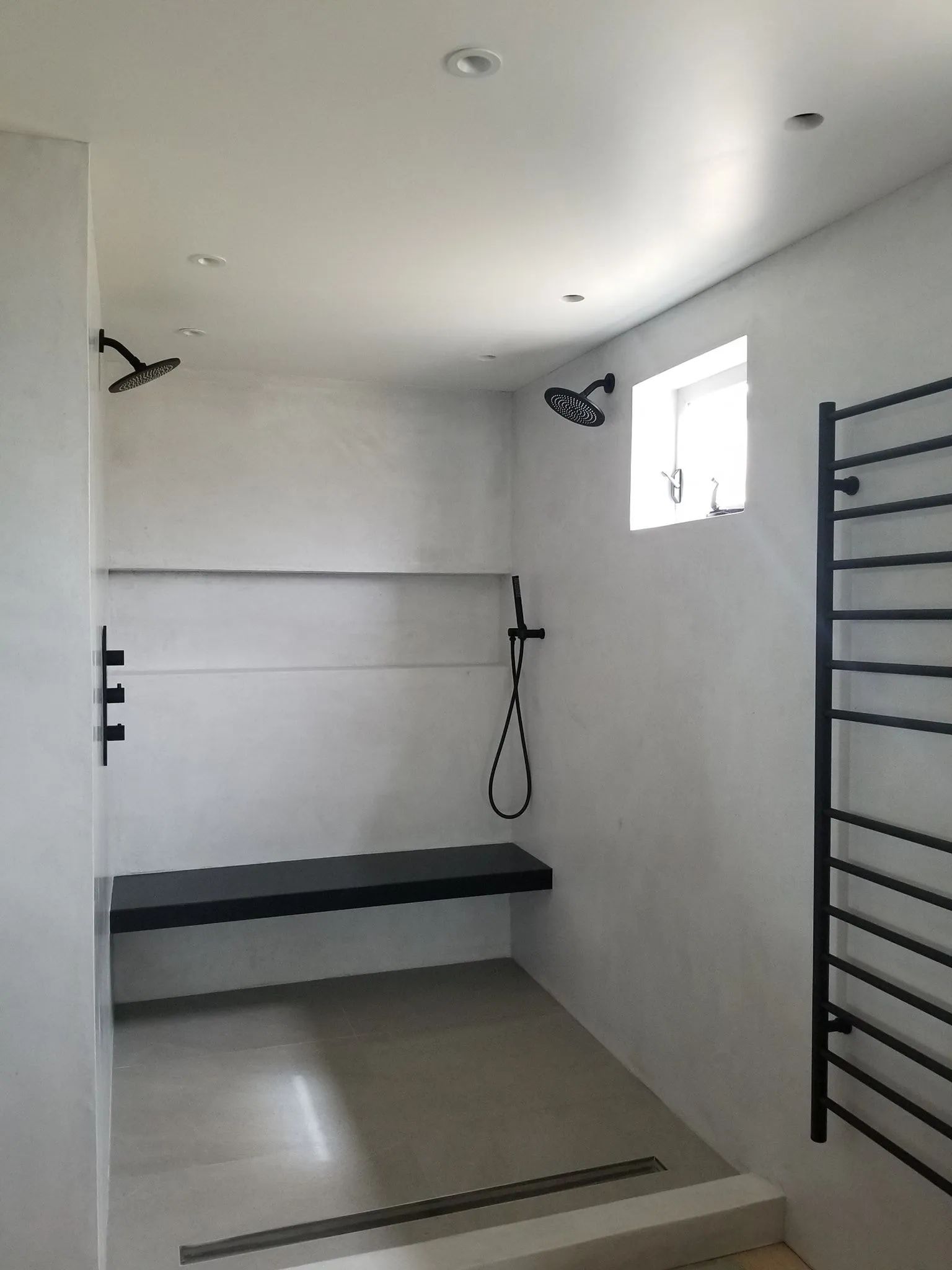 Small white bathroom with shower bench, wall bars, and window.