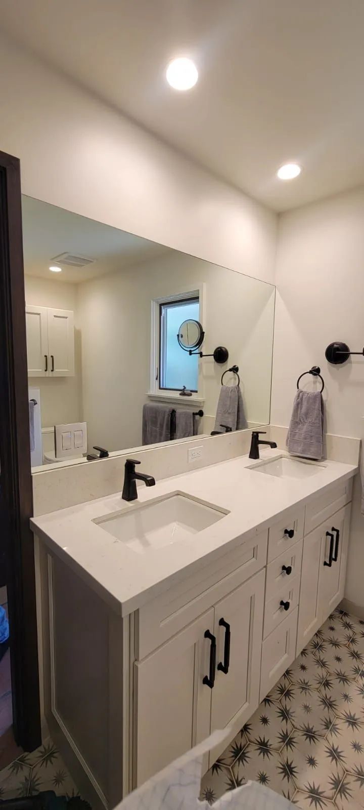 Modern bathroom vanity with double sinks, large mirror, black fixtures, and patterned tile floor.