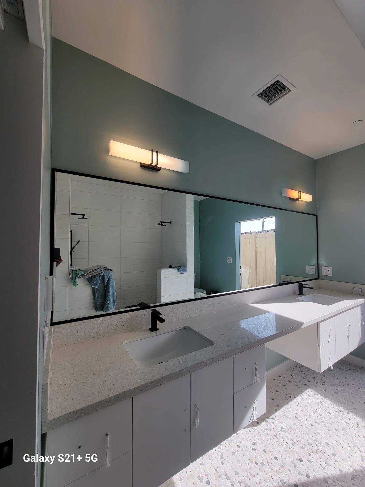 Modern bathroom with double sinks, large mirror, and mint-green walls.