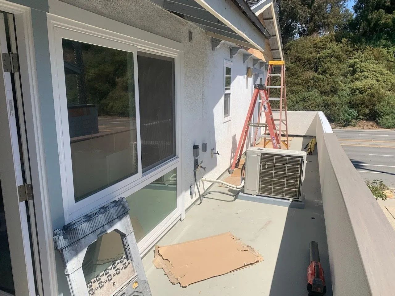 Patio beside a house under repair, with ladder, tools, and window coverings along the wall