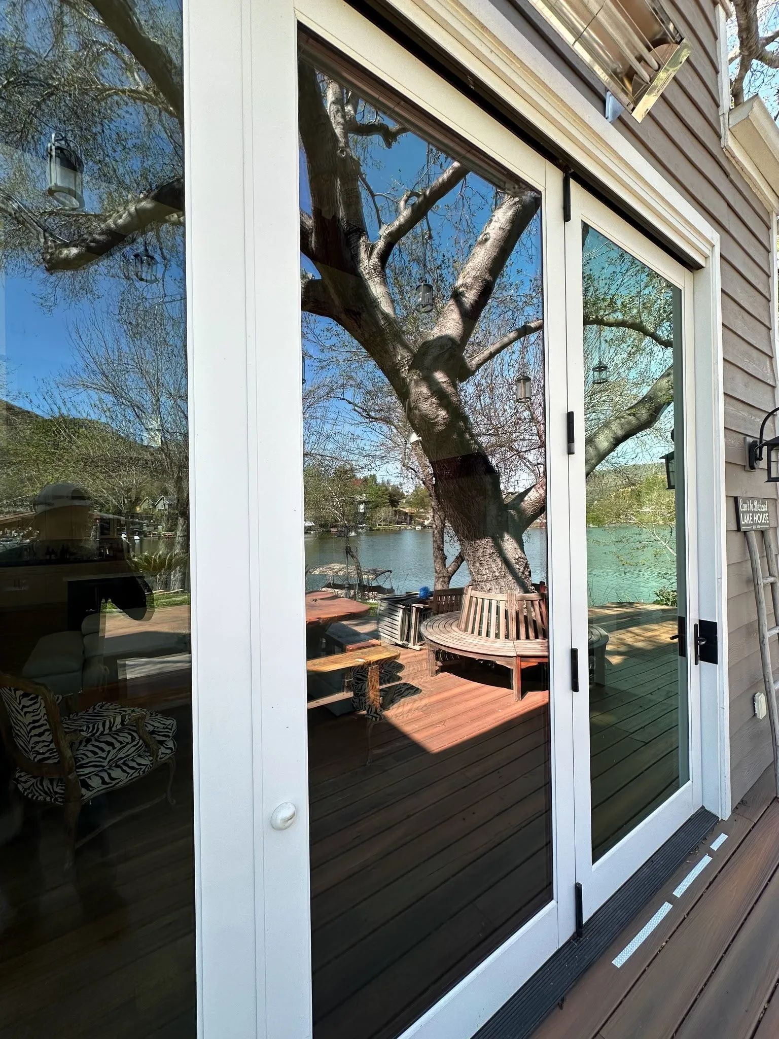 Sliding glass doors reflecting a tree and deck overlooking a lake