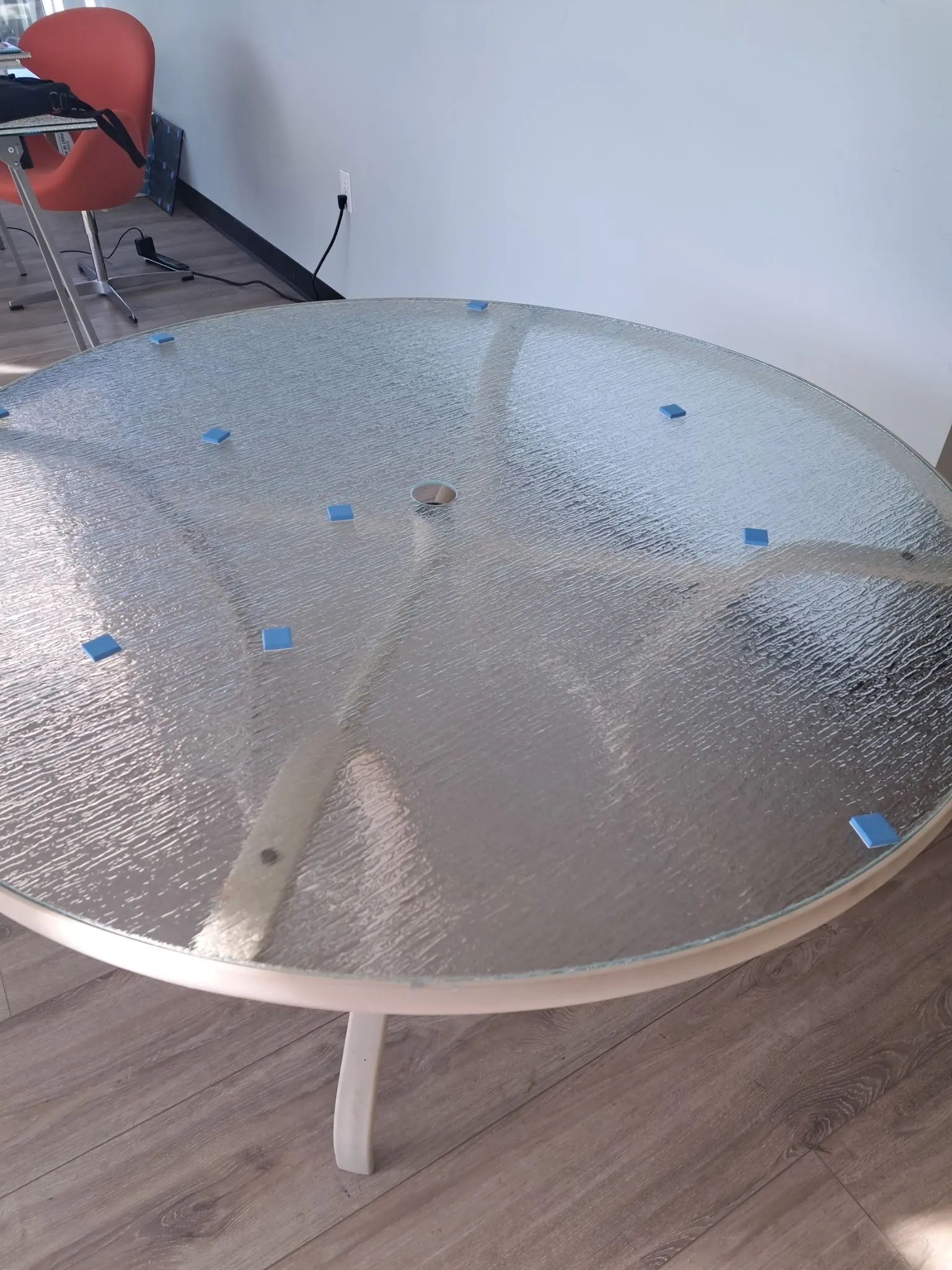 Round frosted glass table with metal legs in a room, with red chair and wooden floor in the background
