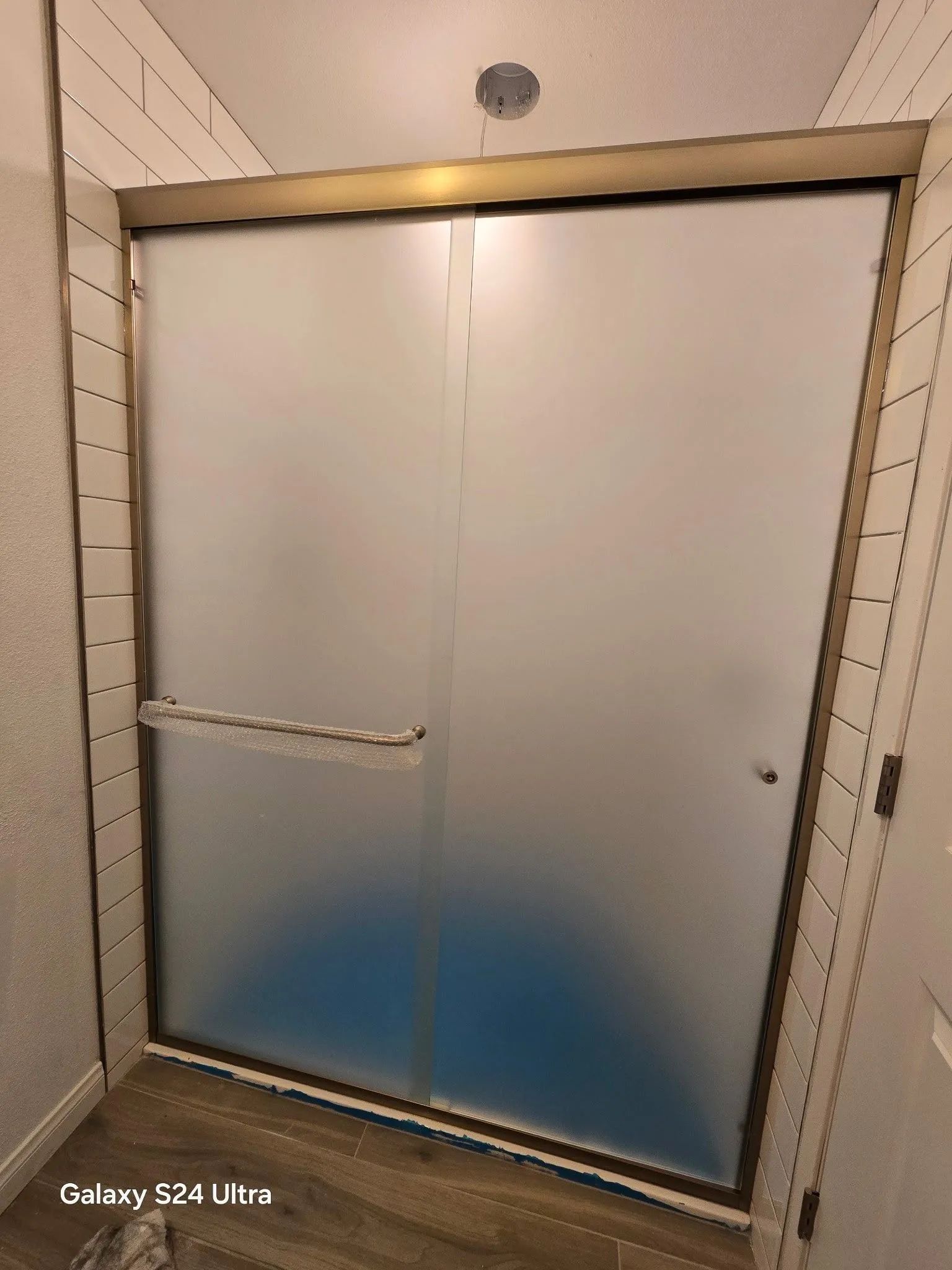 Fogged shower door with blue stain at the bottom in a tiled bathroom.