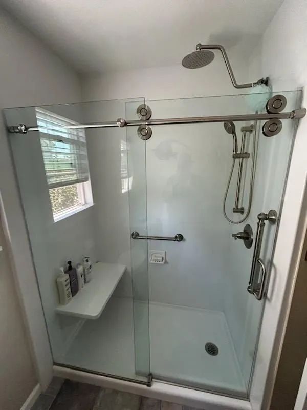 Glass walk-in shower with chrome fixtures, white tile, and a built-in corner shelf.