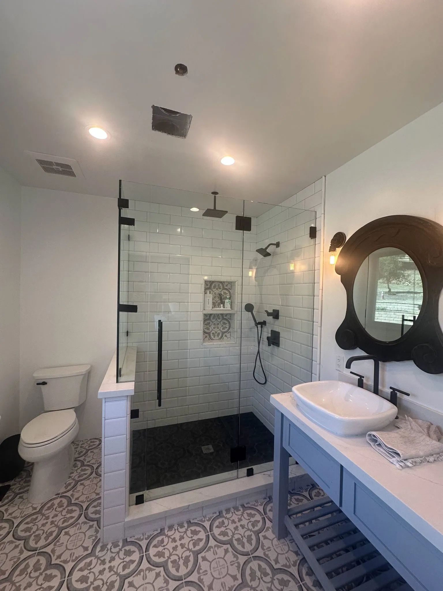 Modern bathroom with glass shower, white tile, pedestal sink, toilet, and patterned floor.