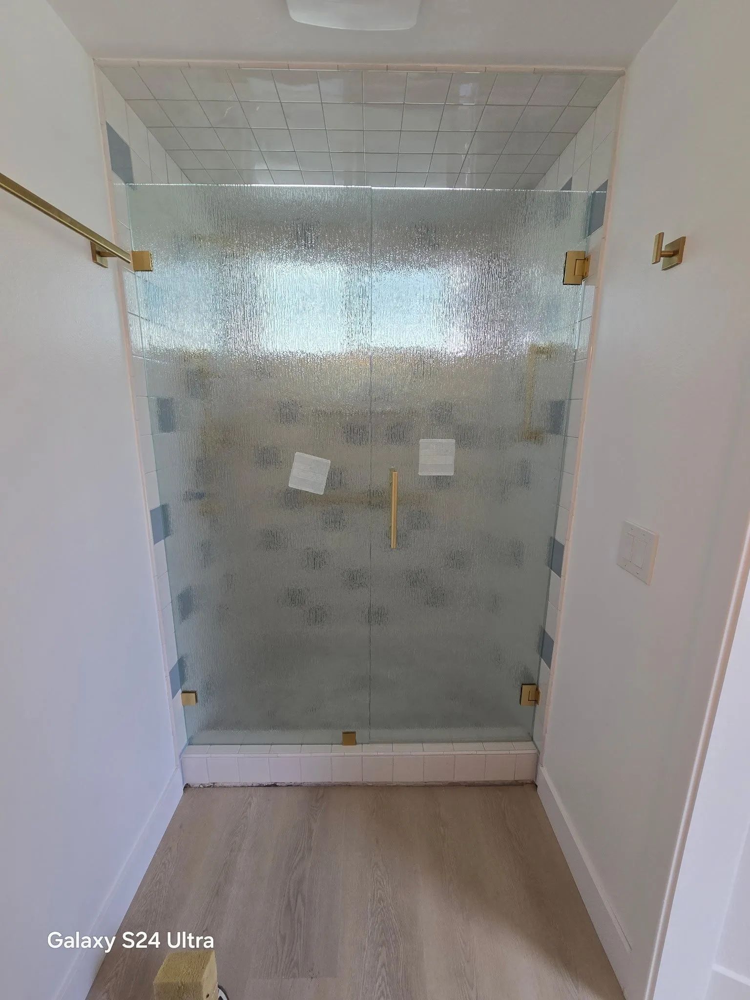 Glass shower enclosure in a bright bathroom with white walls and light wood floor