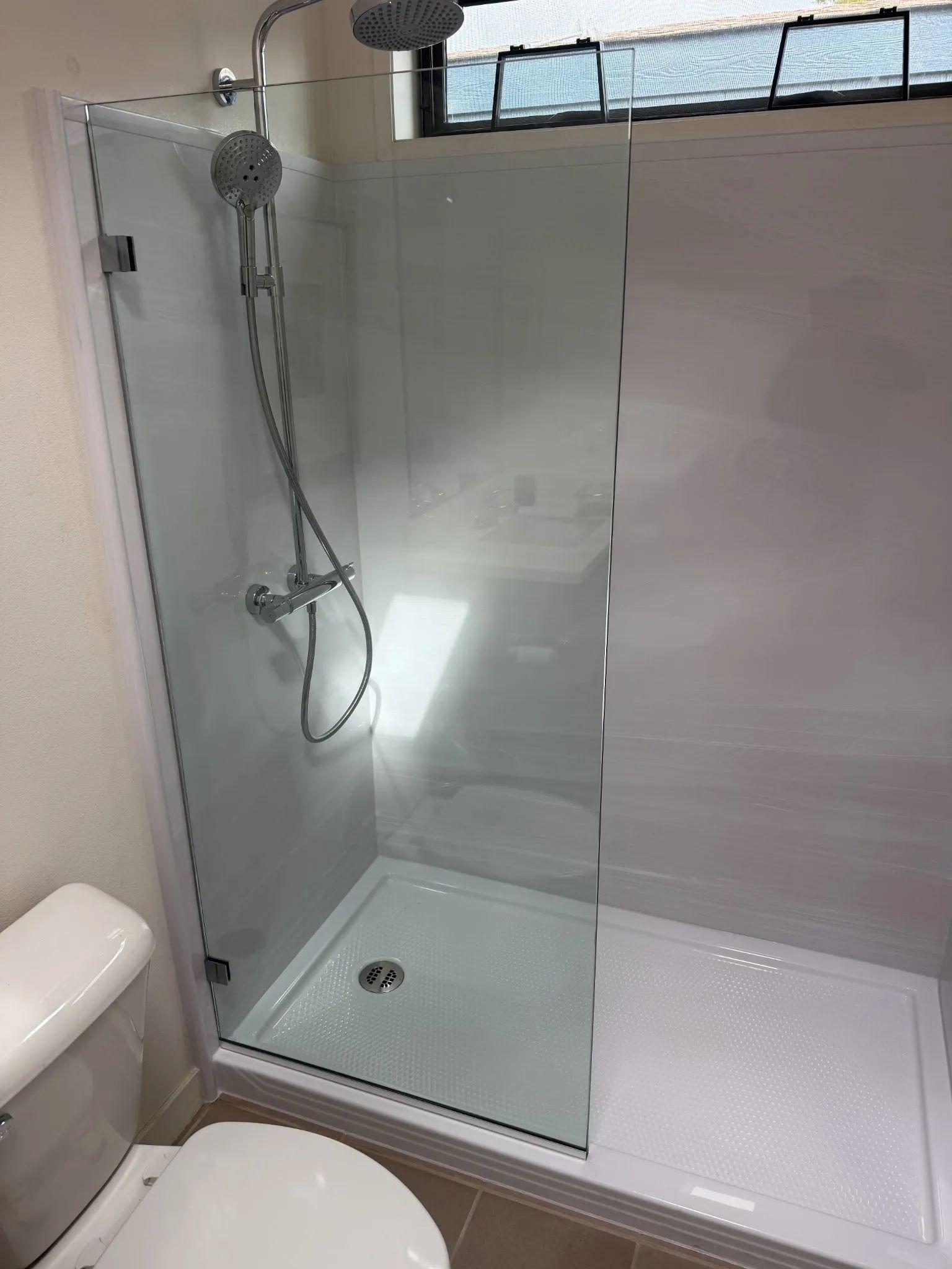 Modern tiled bathroom with glass walk-in shower, wall-mounted showerhead, and white toilet edge visible