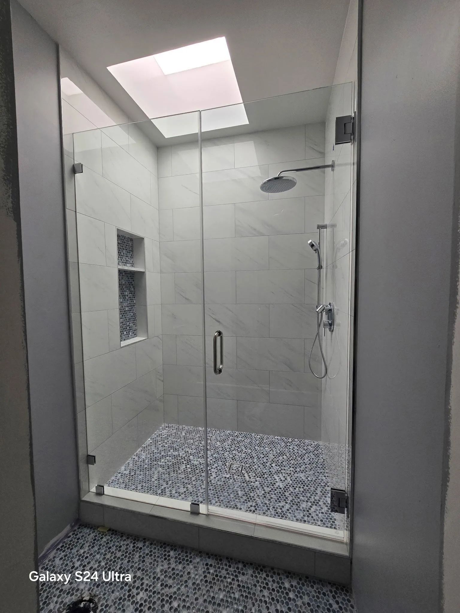 Modern glass shower enclosure with tiled walls and a mosaic floor under a skylight