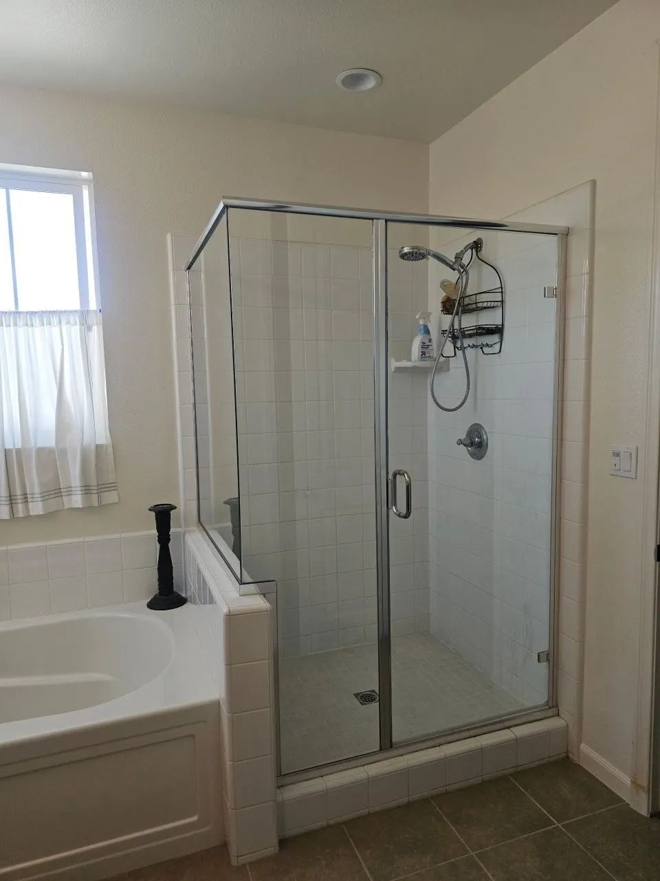 Bathroom with glass walk-in shower next to a white bathtub and window with sheer curtains.