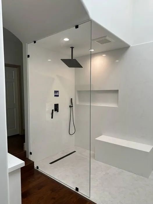 Modern white bathroom with glass shower enclosure, black fixtures, and wood flooring