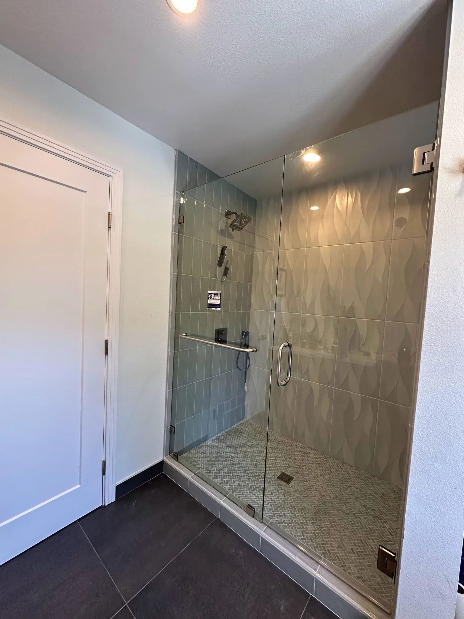 Small bathroom with dark tile floor, glass shower enclosure, and white door beside it.