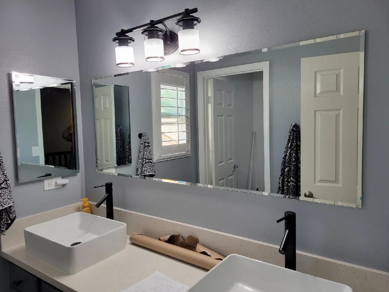 Bright bathroom with double mirrors, white vessel sink, black fixtures, and a glass shower door.