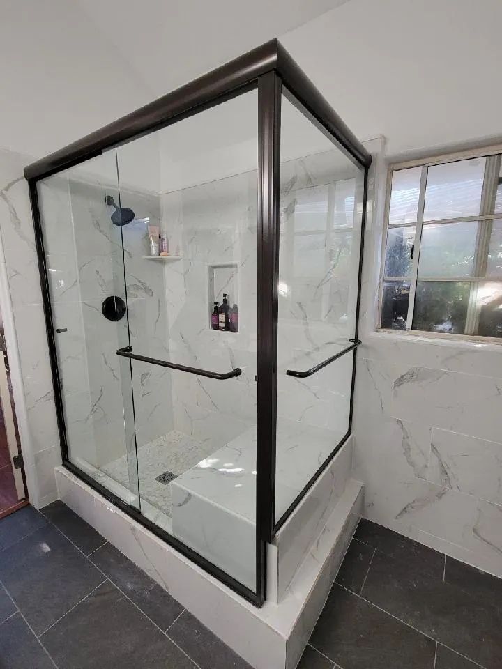 Glass shower enclosure with black trim in a tiled bathroom.