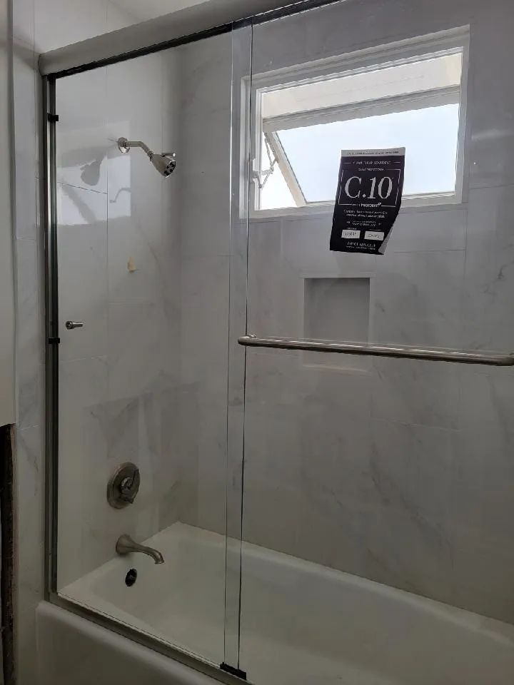 White bathroom with a glass-enclosed bathtub/shower, chrome fixtures, and a small window.