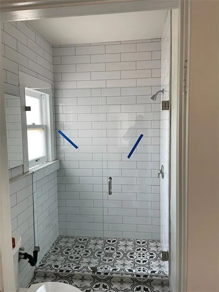 Small tiled shower stall with patterned floor and a window on the left.