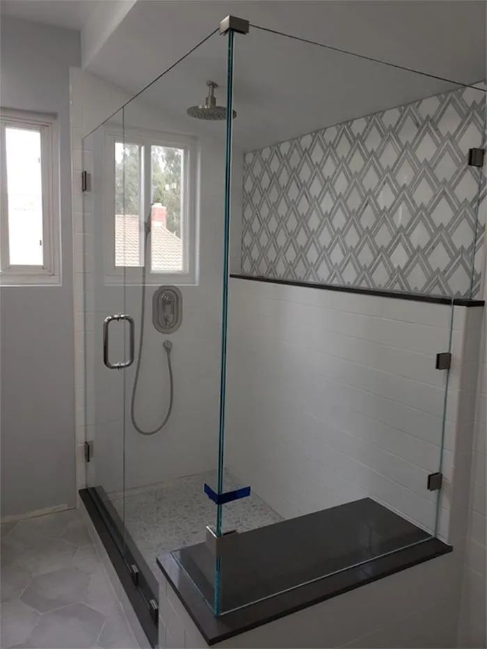 Modern bathroom shower with glass enclosure, rainfall showerhead, grab bar, and patterned wall tiles