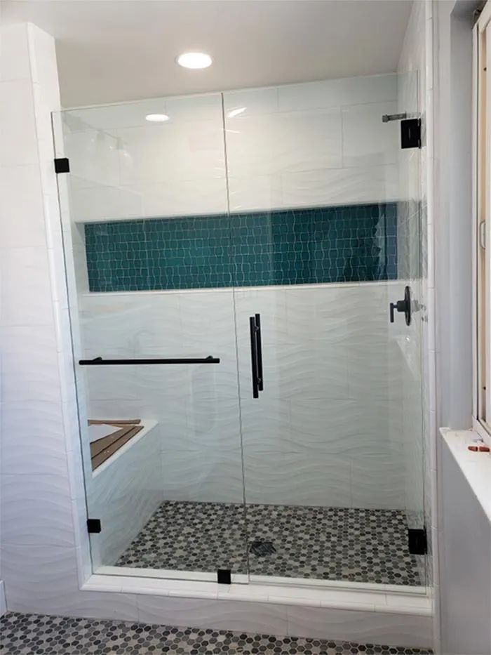 Modern glass shower with teal tile accent wall and patterned pebble floor