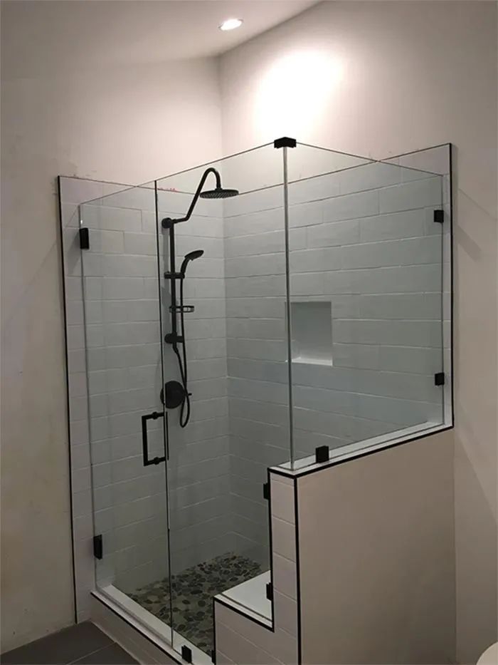 Glass shower enclosure with black fixtures and pebble floor in a tiled bathroom