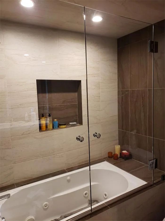 Modern bathroom with glass shower wall, white soaking tub, and beige tile walls