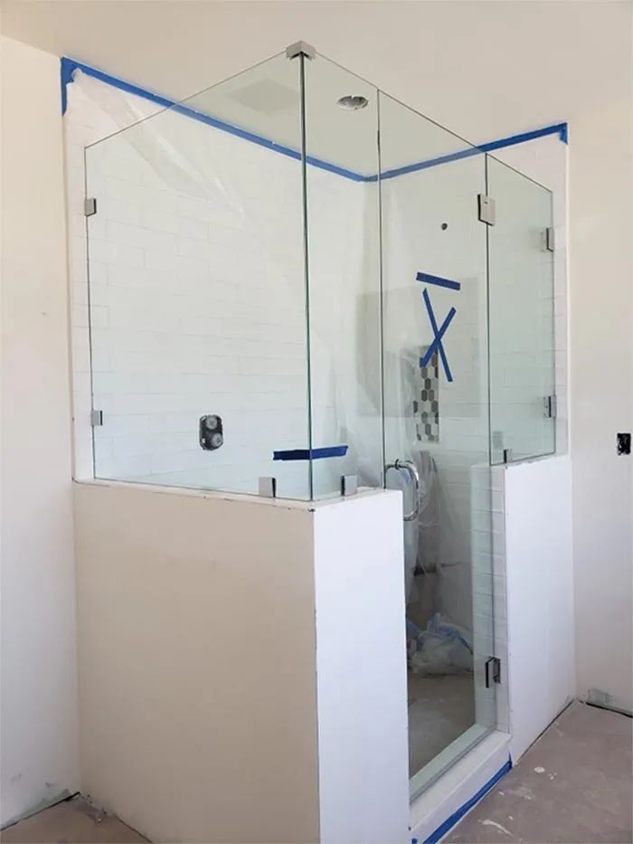 Glass shower enclosure with blue painter’s tape in an unfinished bathroom area