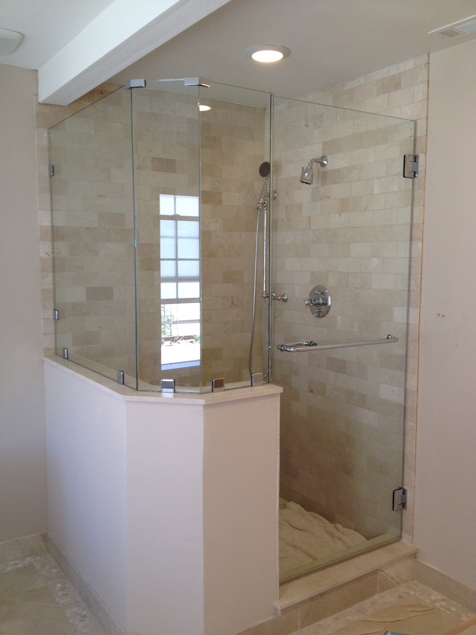 Glass-enclosed tiled shower with white half wall in a bright bathroom