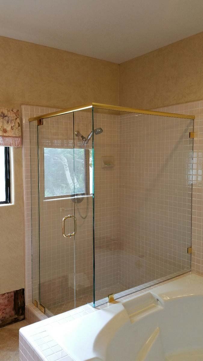 Glass shower enclosure beside a white bathtub in a beige bathroom