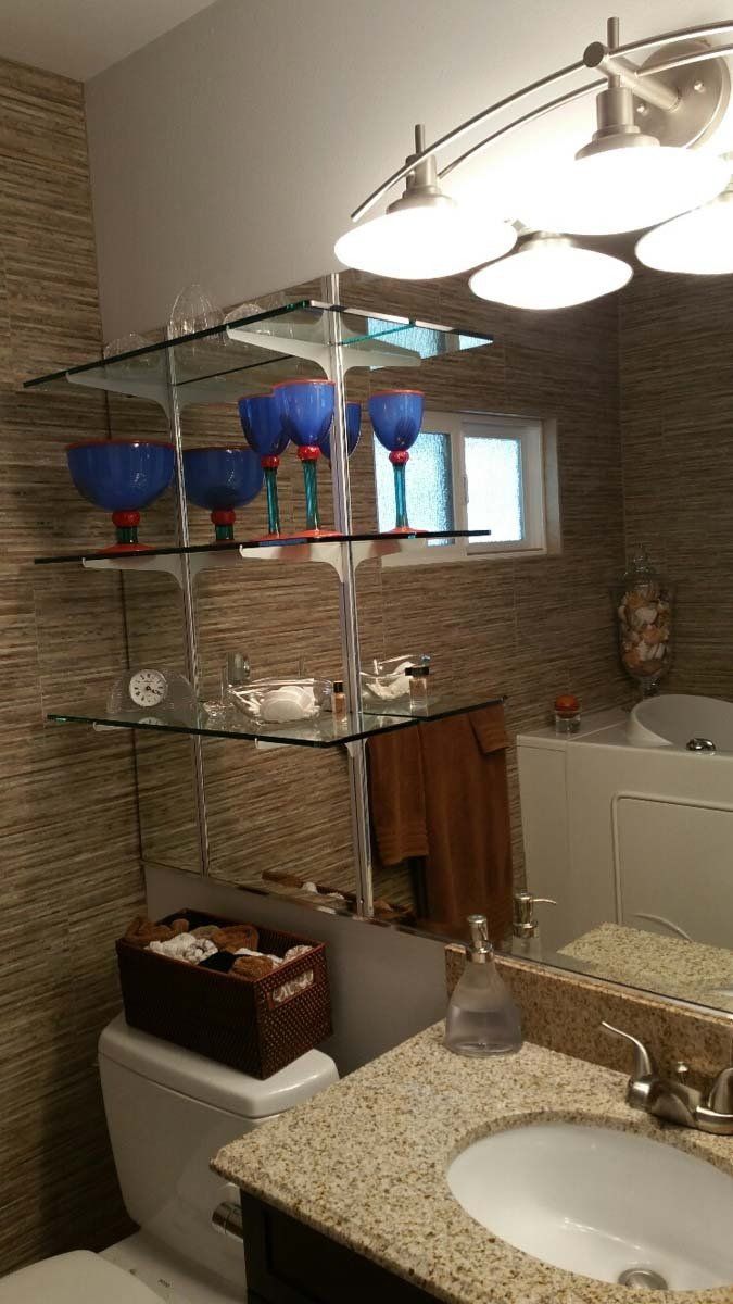 Bathroom with glass shelves, vanity sink, mirror, and blue-red decorative glasses on top.