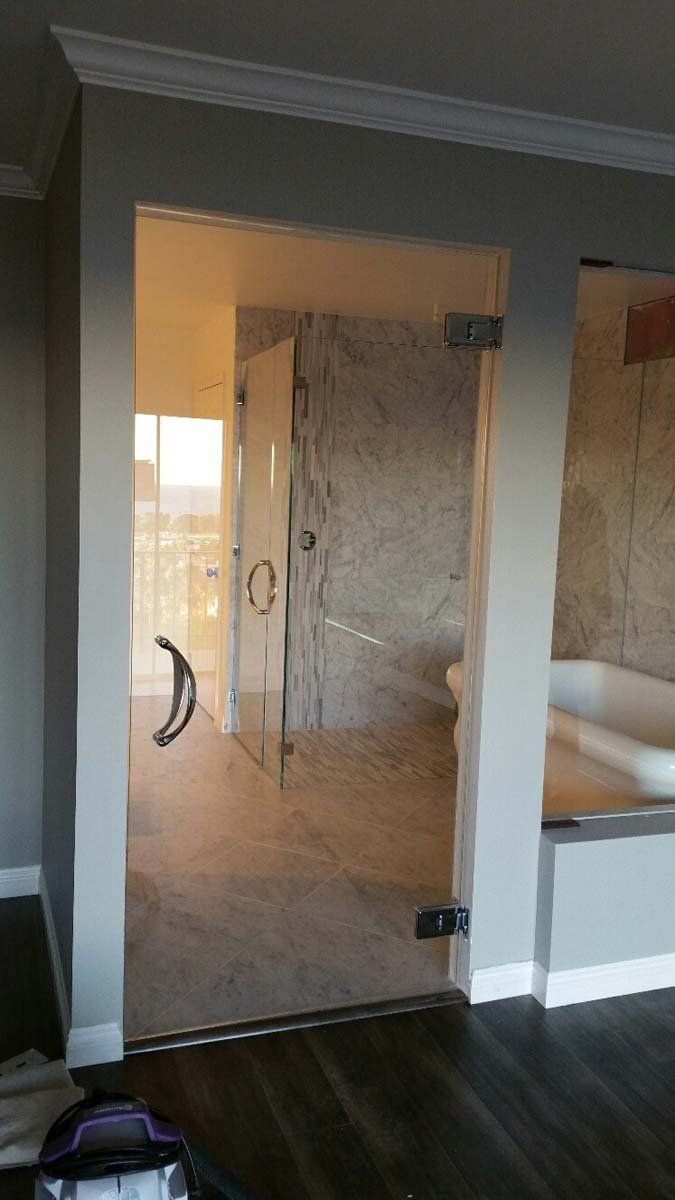 Interior view of a bathroom with a glass shower door, marble walls, and a sink on the right.