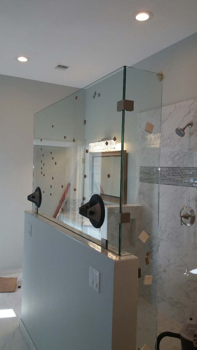 Glass shower enclosure in a tiled bathroom with a frosted lower panel and towel bars nearby
