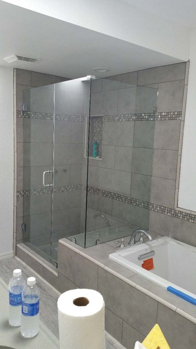 Bathroom with glass shower enclosure, tiled wall, bathtub, and toiletries on a counter.