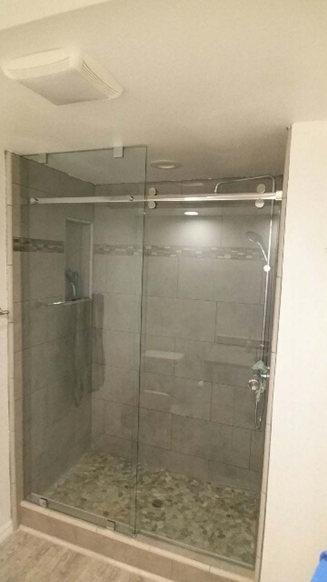 Glass walk-in shower with gray tile and a pebble stone floor in a bathroom