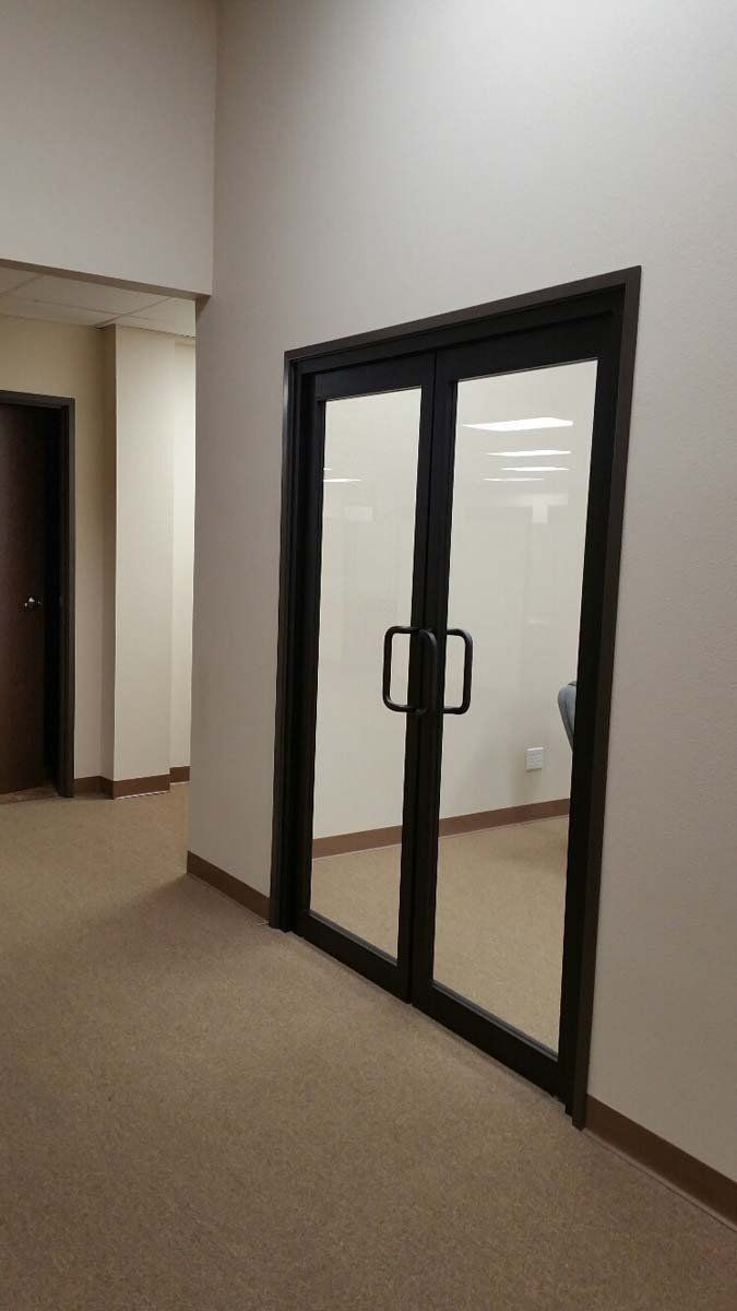 Empty office hallway with black-framed glass double doors and beige carpet