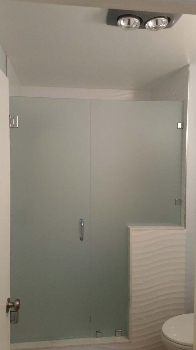 Modern bathroom with frosted glass shower, toilet partially visible, and ceiling light above