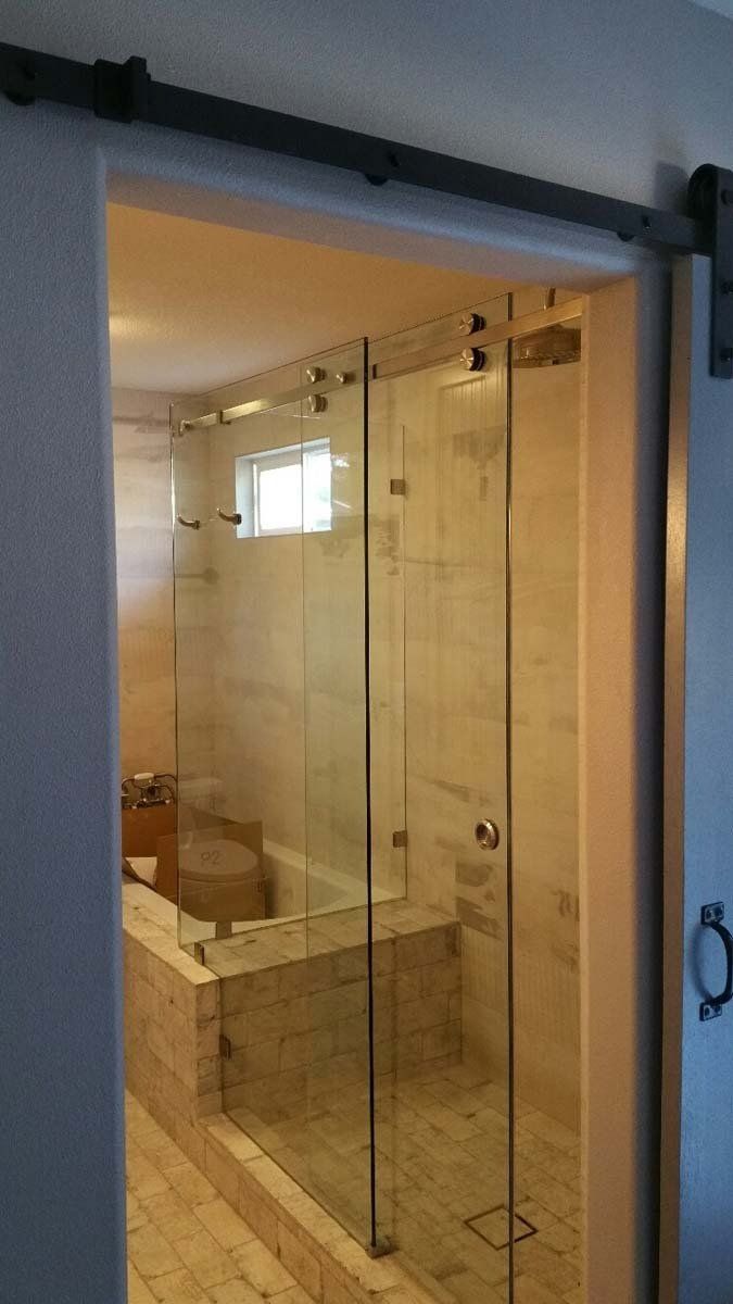 Glass shower enclosure in a beige-tiled bathroom with a small window and chrome fixtures