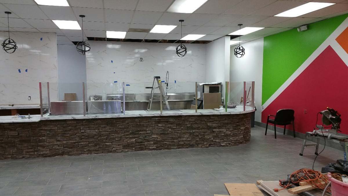 Empty restaurant counter with glass sneeze guards, tiled floor, and a bright green-and-pink wall.