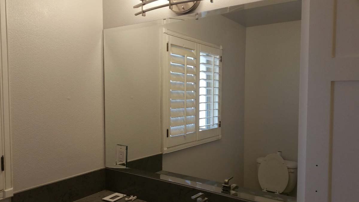 Bathroom with sink, mirror, white shutters, and a toilet in the background.