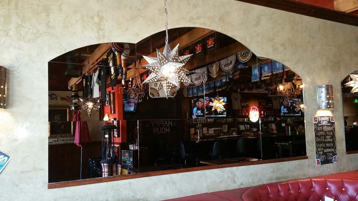 Bar interior seen through an arched opening, with hanging star lights, bottles, and red seating