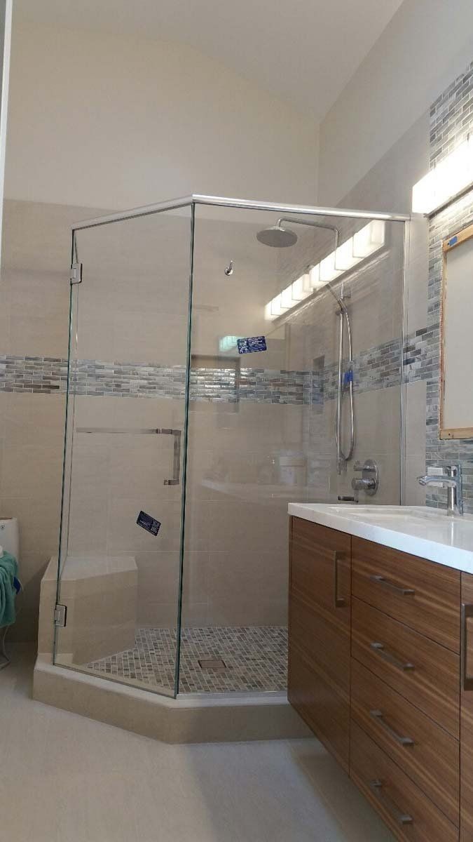 Glass shower enclosure in a bright bathroom beside a wooden vanity and mirror.