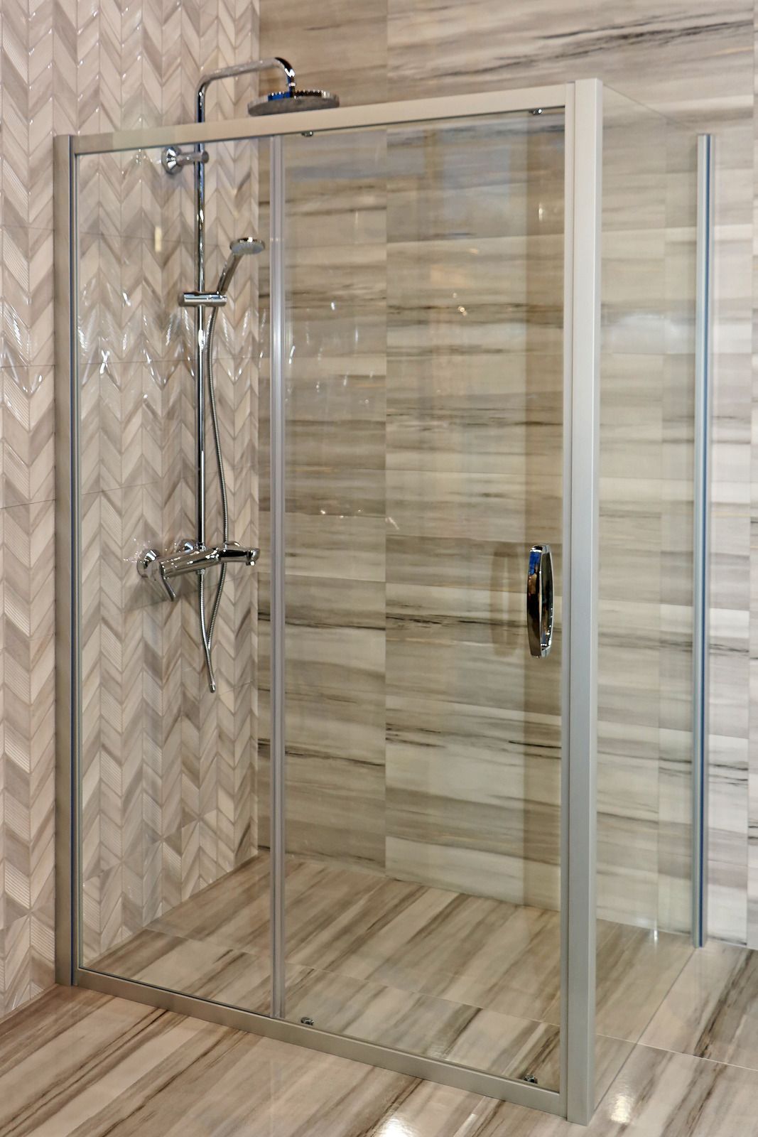 Shower stall with glass doors, silver fixtures, and marble-like tile walls and floor.