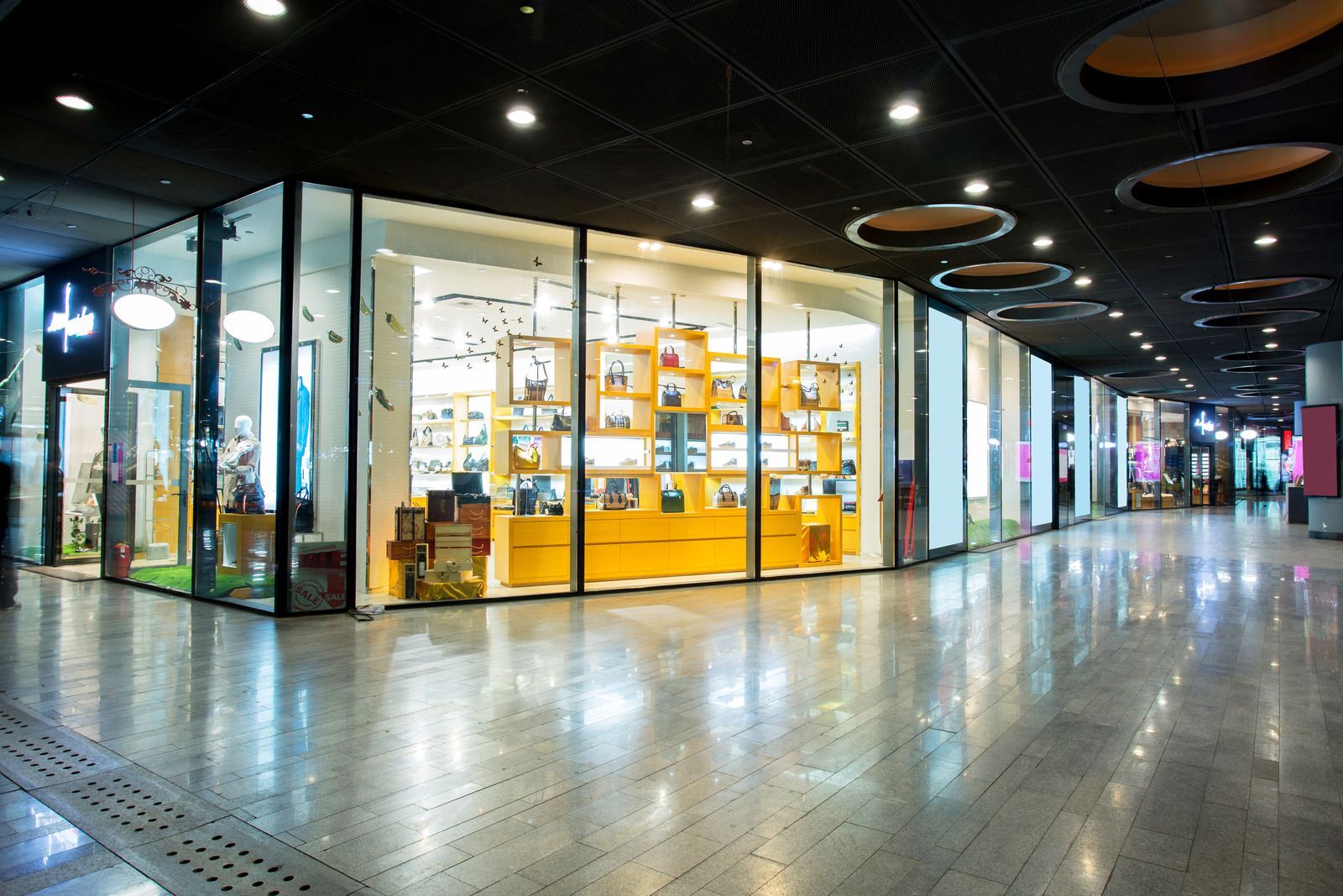 Shopping mall interior with bright yellow store, glass storefront, and polished floor.