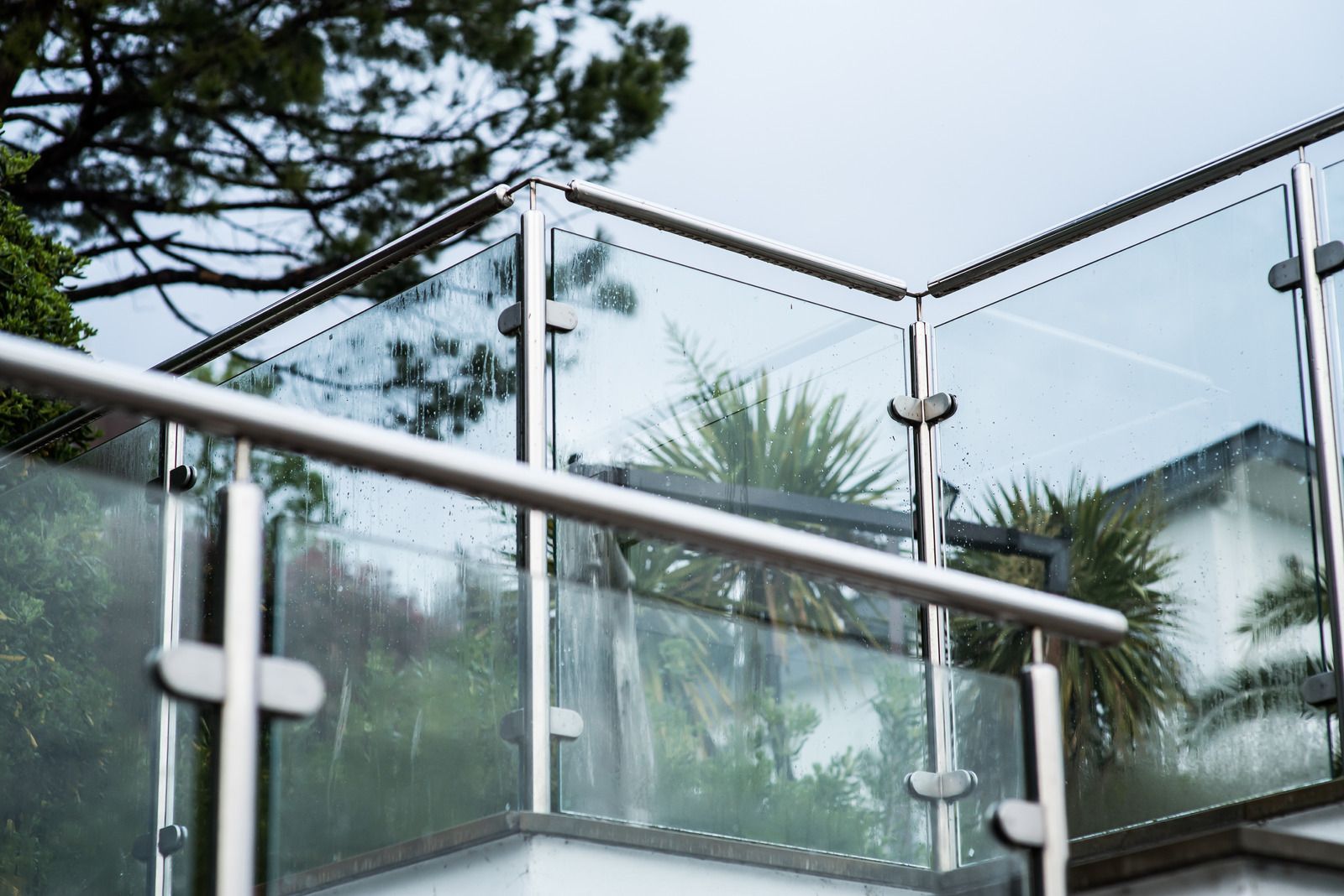 Glass and stainless steel balcony railing overlooking greenery on a cloudy day.