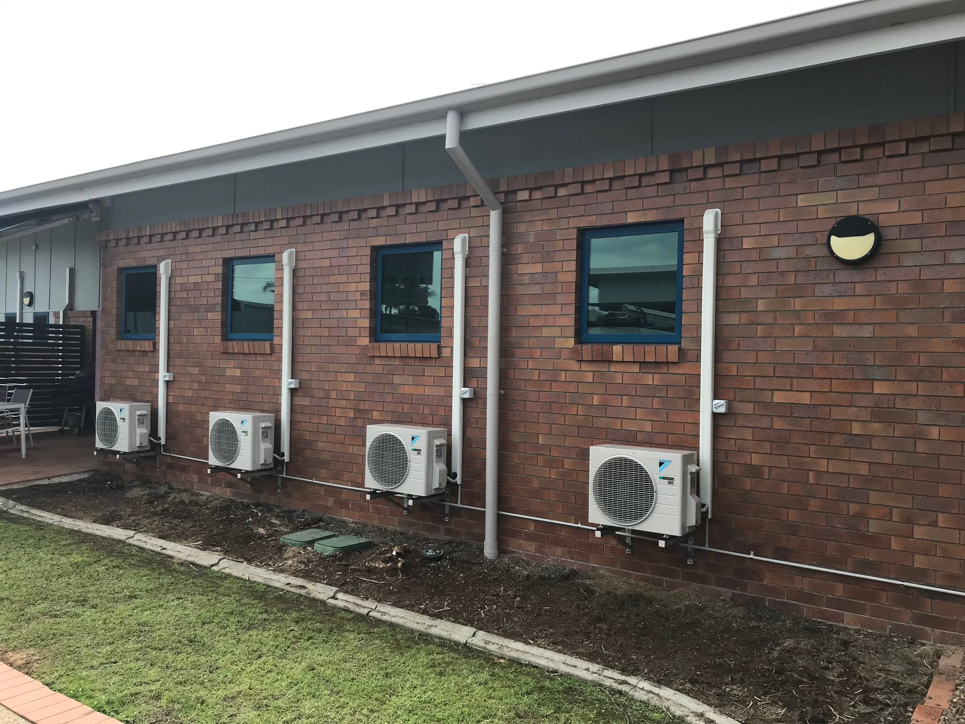 Brick building exterior with several wall-mounted air conditioning units and small windows under an overhang